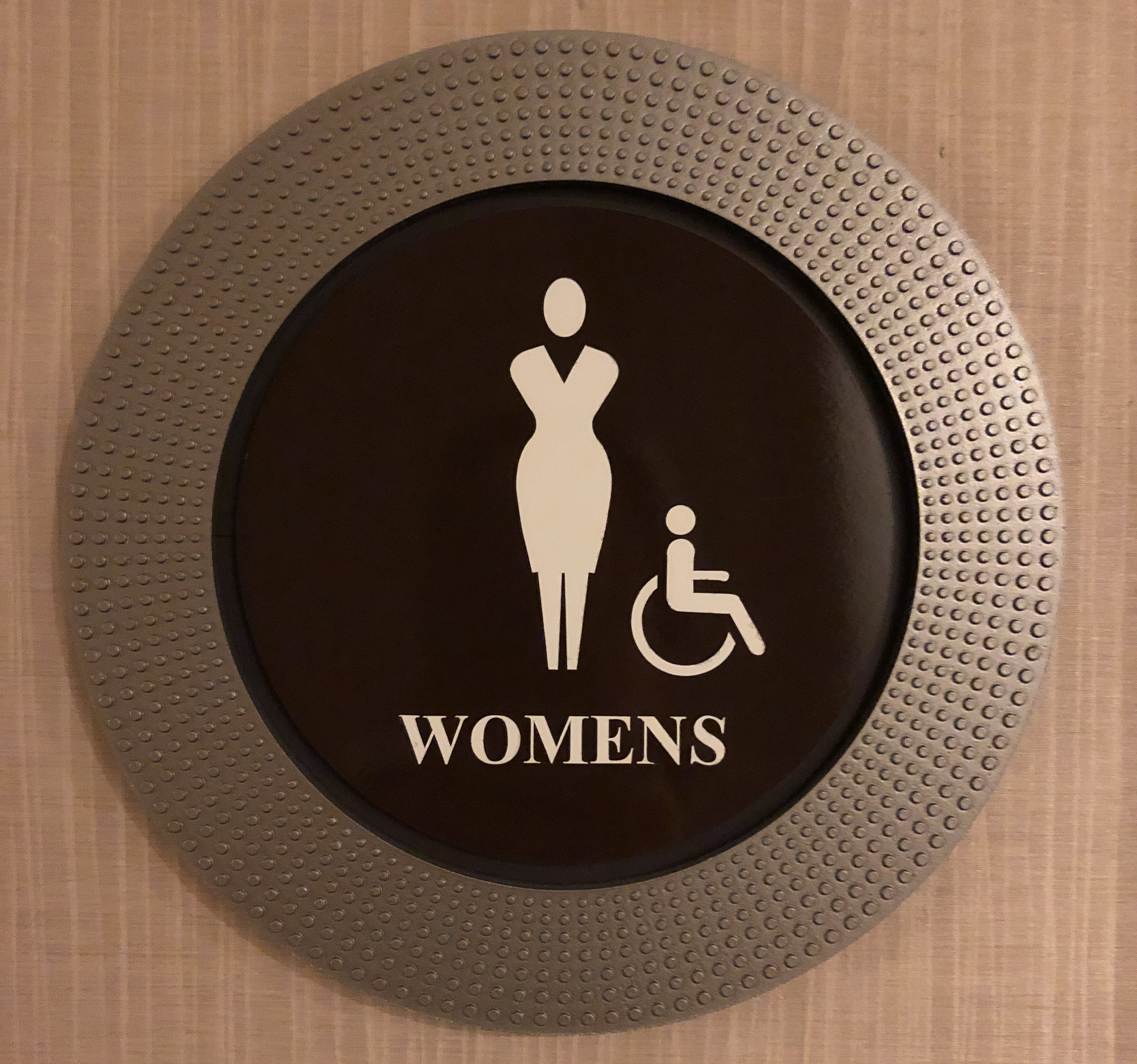 brown circular plate with a figure with a head and face with no features, no hair, curvy figure in a dress, the word "womens" and a figure sitting in a wheelchair