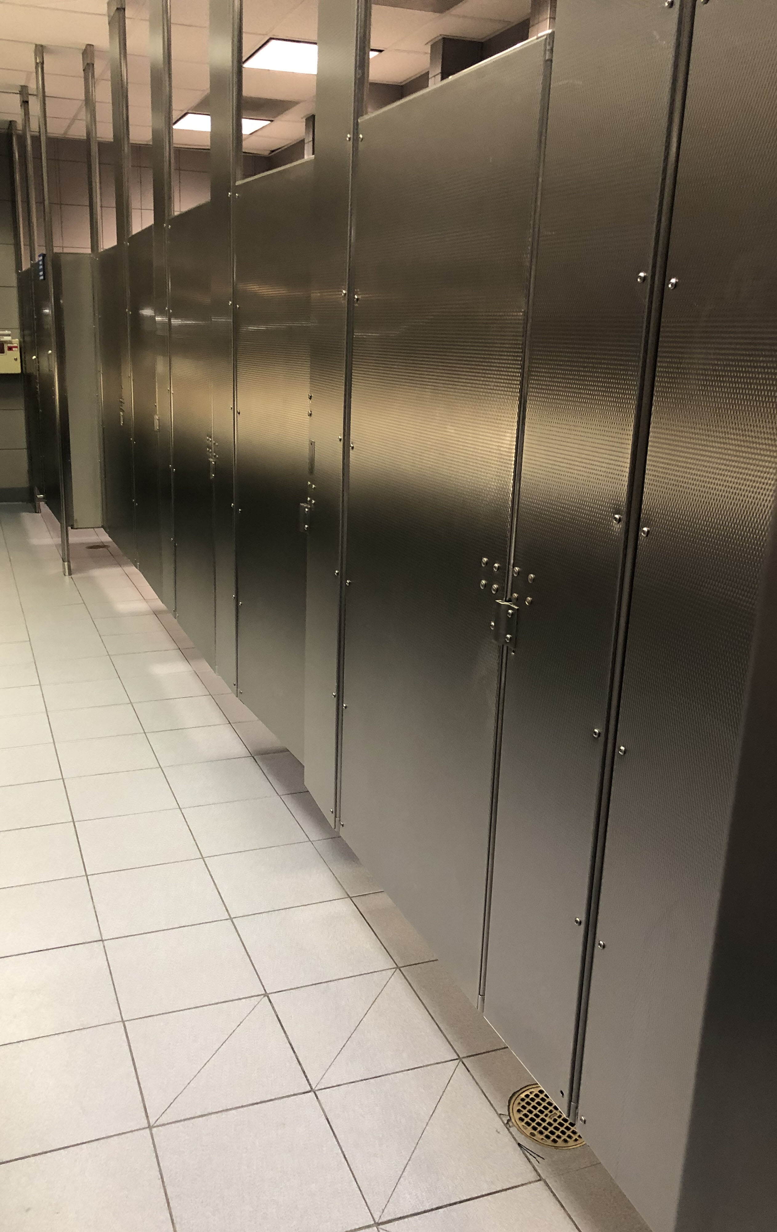 a bank of 8 restroom stalls, all with the doors closed, all low to the ground, no door handles, silver metal