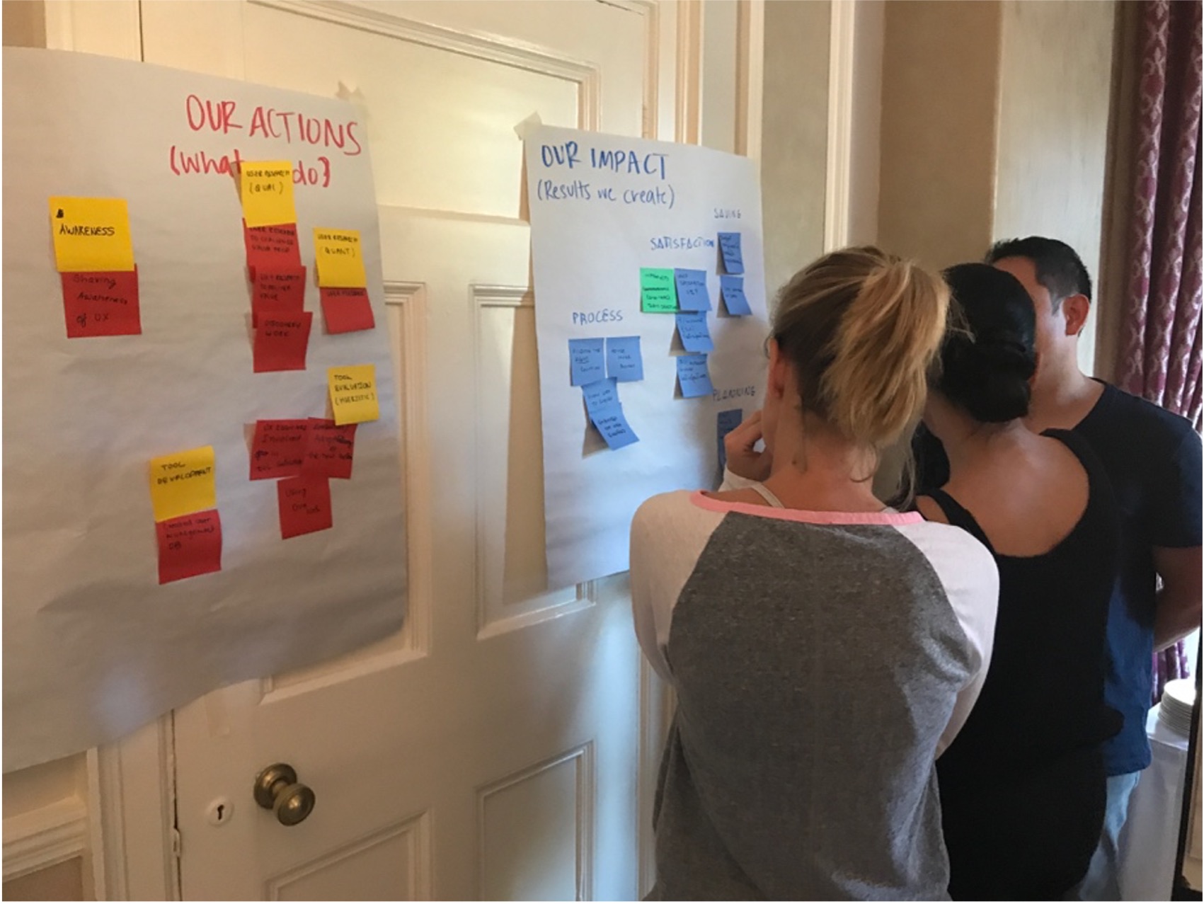 3 teams members standing in front of a poster on a wall, discussing their value elements