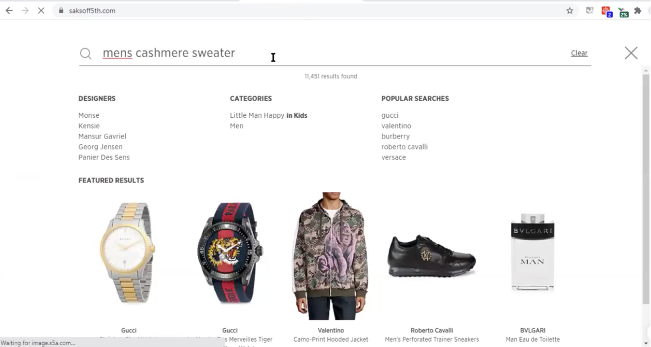 The site search on saksoff5th.com: The search bar contains the query “mens cashmere sweaters.” At the bottom of the container, a featured results section contains a row of image-based products, including watches, a jacket, shoes and cologne.