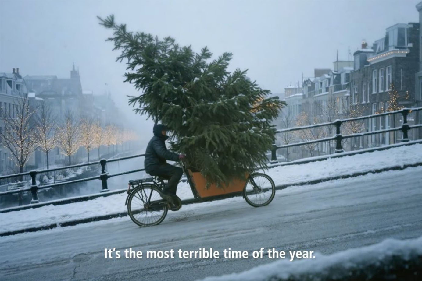 A screenshot of McDonald’s AI-generated ad depicting a cyclist struggles uphill through snow on a cargo bike carrying an oversized Christmas tree, with on-screen text reading, “It’s the most terrible time of the year.”