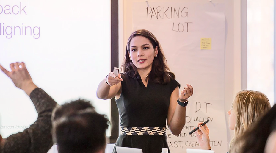 An instructor leads a custom UX workshop, presenting to participants and answering questions in a classroom setting.